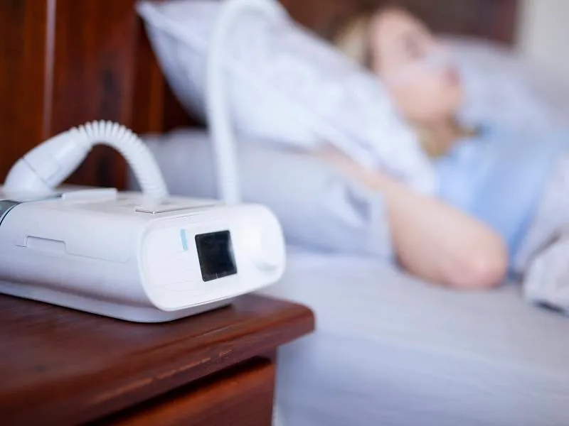 CPAP machine on a nightstand beside a sleeping patient