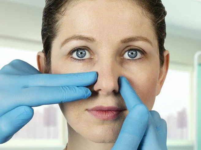 Gloved hands examining a patient’s nose